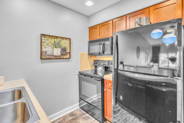 kitchen with hardwood / wood-style flooring, sink, black appliances, and tasteful backsplash