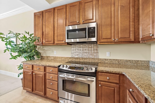 kitchen with light stone countertops, light tile patterned floors, appliances with stainless steel finishes, and crown molding