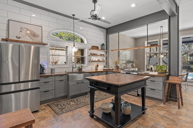 kitchen with sink, gray cabinets, pendant lighting, ceiling fan, and stainless steel appliances