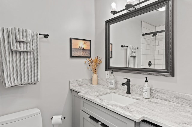 bathroom featuring tiled shower, vanity, and toilet