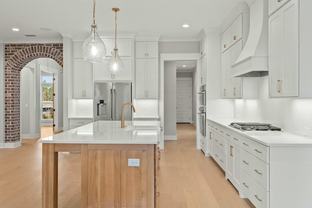 kitchen with premium range hood, pendant lighting, sink, a kitchen island with sink, and appliances with stainless steel finishes