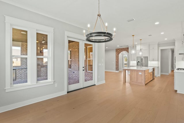 kitchen with an island with sink, stainless steel refrigerator with ice dispenser, brick wall, hanging light fixtures, and white cabinets