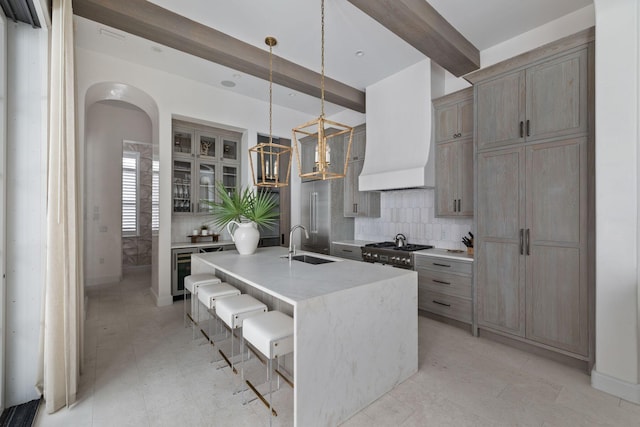 kitchen featuring a kitchen island with sink, custom range hood, pendant lighting, beam ceiling, and sink