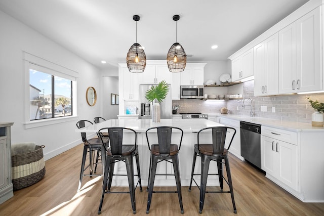 kitchen featuring a kitchen island, sink, hanging light fixtures, appliances with stainless steel finishes, and white cabinets