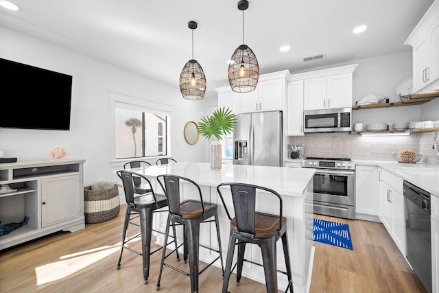 kitchen with appliances with stainless steel finishes, a kitchen island, decorative light fixtures, white cabinetry, and decorative backsplash