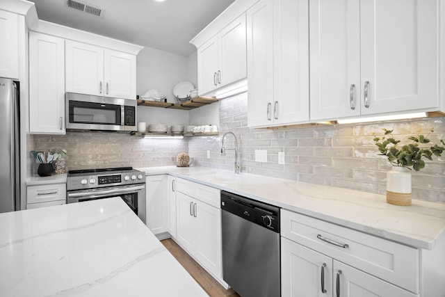 kitchen with stainless steel appliances, white cabinets, and light stone counters