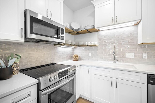 kitchen with light stone countertops, white cabinetry, stainless steel appliances, sink, and backsplash