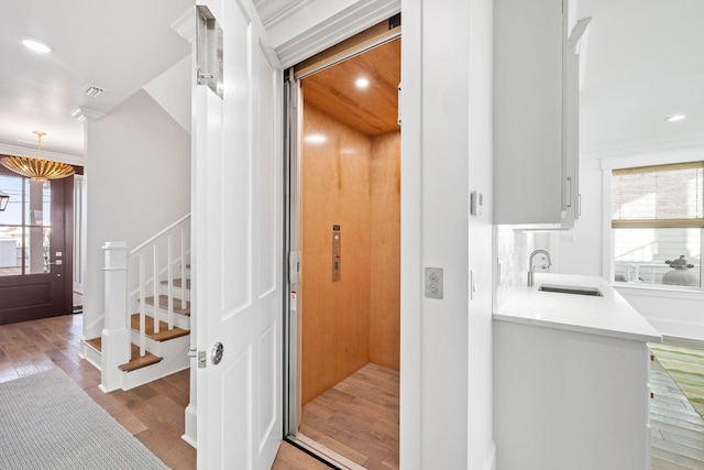 bathroom with wood-type flooring, sink, crown molding, and elevator