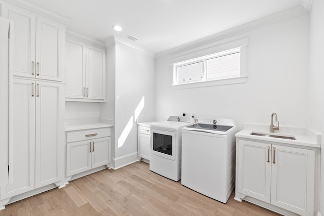 washroom featuring sink, washing machine and clothes dryer, light wood-type flooring, ornamental molding, and cabinets