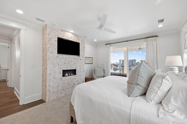 bedroom featuring ceiling fan, hardwood / wood-style floors, crown molding, and a fireplace