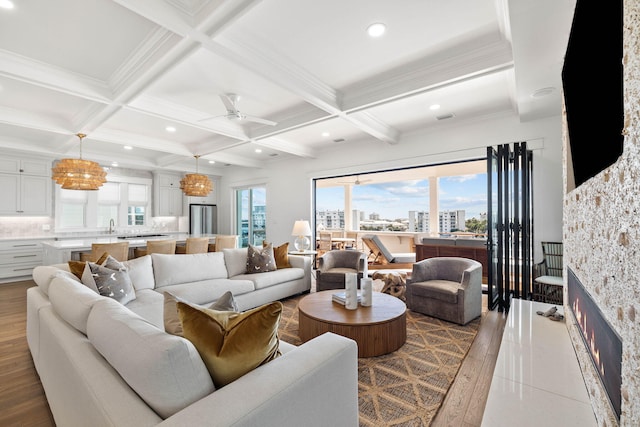 living room with light hardwood / wood-style flooring, ceiling fan with notable chandelier, coffered ceiling, and beamed ceiling