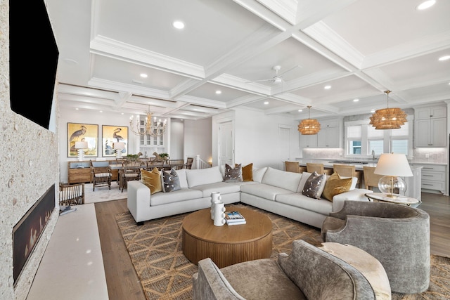 living room featuring ceiling fan, dark hardwood / wood-style flooring, coffered ceiling, and a stone fireplace