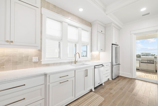 kitchen with white cabinetry, appliances with stainless steel finishes, ornamental molding, light hardwood / wood-style flooring, and sink