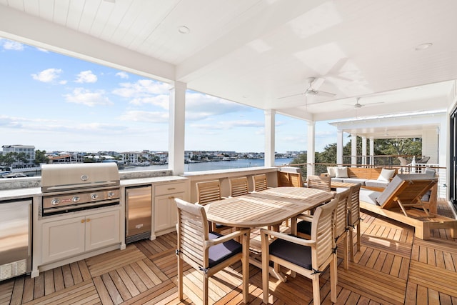 wooden terrace with exterior kitchen, a grill, a water view, ceiling fan, and an outdoor hangout area