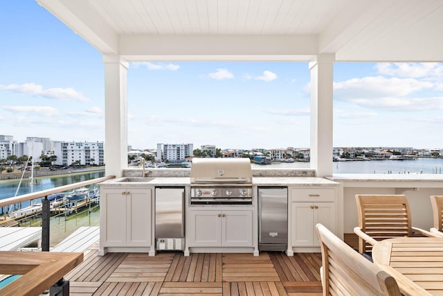 exterior space featuring a grill, sink, a balcony, a water view, and an outdoor kitchen