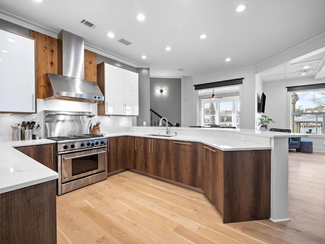 kitchen with stainless steel gas range oven, visible vents, wall chimney exhaust hood, modern cabinets, and white cabinetry