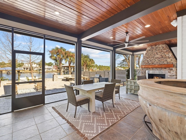 sunroom featuring a stone fireplace, a water view, wood ceiling, a ceiling fan, and beam ceiling