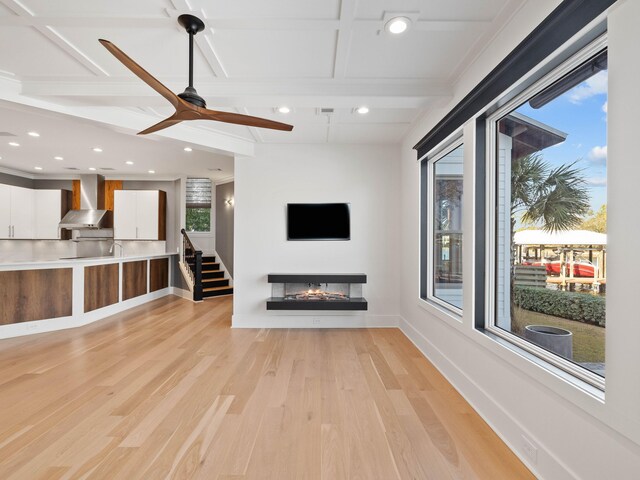 unfurnished living room with stairway, light wood-style flooring, a multi sided fireplace, ceiling fan, and baseboards