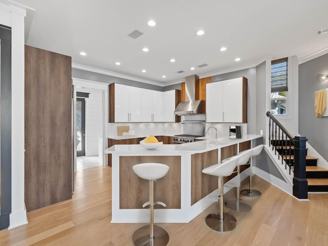 kitchen with a breakfast bar, light countertops, white cabinetry, and wall chimney exhaust hood