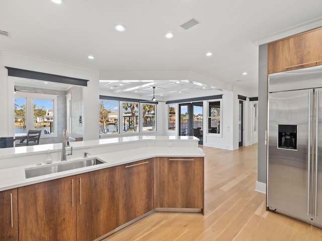 kitchen featuring built in fridge, light countertops, ornamental molding, a sink, and light wood-type flooring