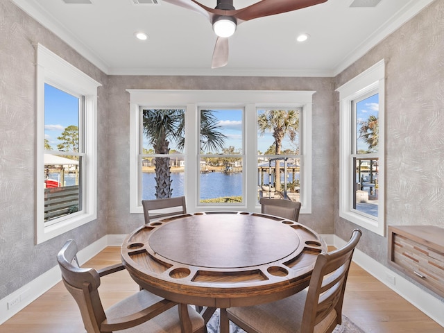 dining space with baseboards, a ceiling fan, a water view, crown molding, and light wood-type flooring