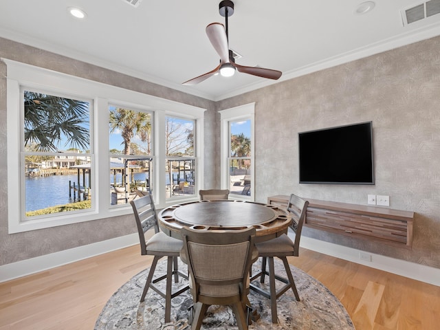 dining area featuring light wood-style flooring, a water view, crown molding, and visible vents