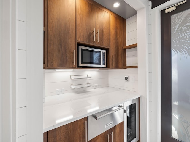 kitchen with beverage cooler, open shelves, stainless steel microwave, and brown cabinetry