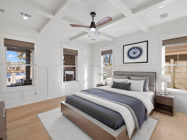 bedroom with beam ceiling, visible vents, a decorative wall, and light wood finished floors