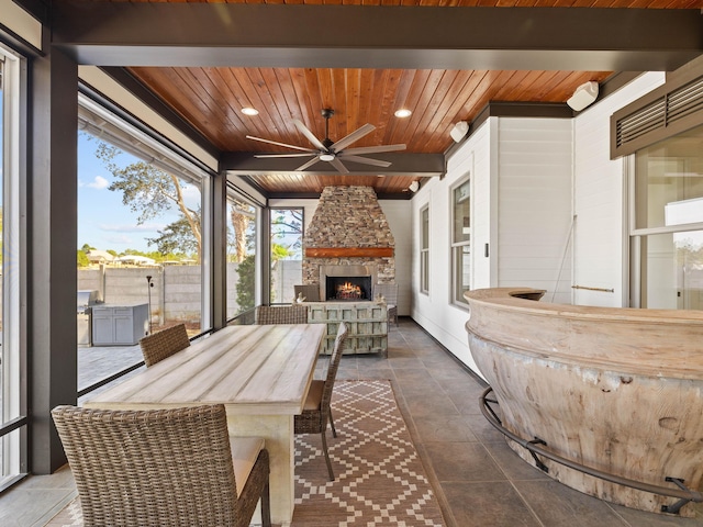 sunroom with beam ceiling, an outdoor stone fireplace, wood ceiling, and a ceiling fan