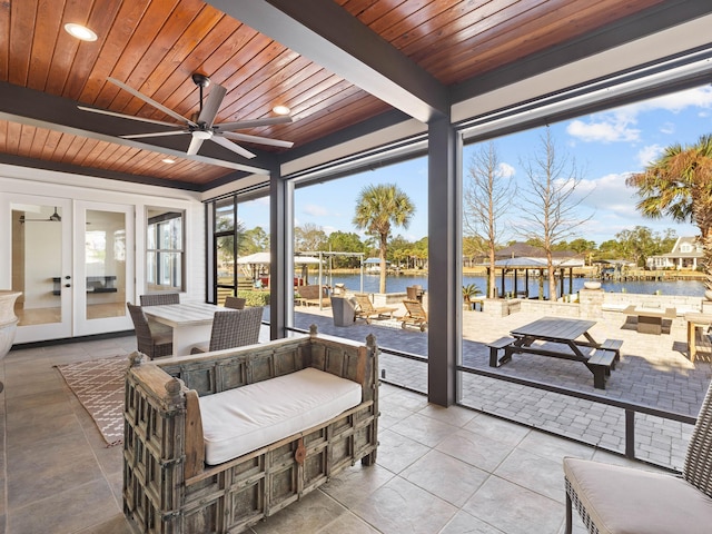 sunroom / solarium featuring a water view, wooden ceiling, a ceiling fan, and beam ceiling