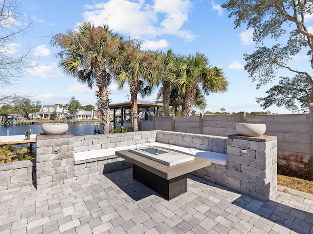 view of patio featuring a water view, an outdoor fire pit, and fence