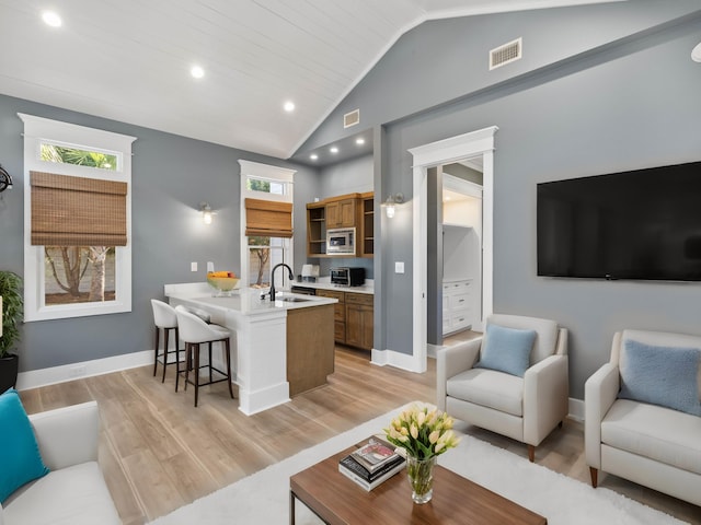 living area featuring vaulted ceiling, light wood-style flooring, visible vents, and a healthy amount of sunlight