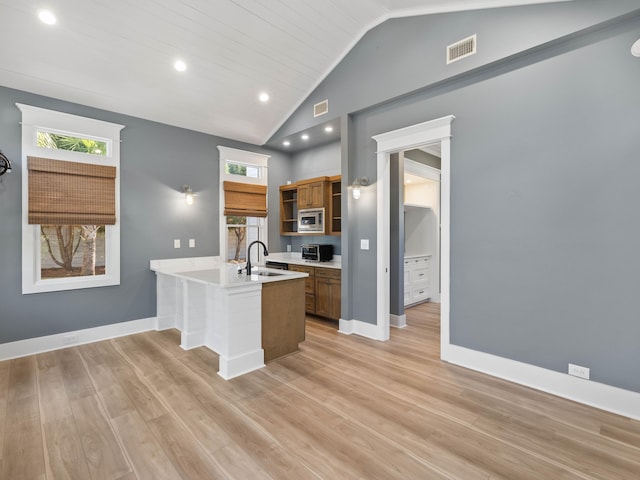 kitchen featuring a peninsula, a sink, light countertops, brown cabinetry, and stainless steel microwave