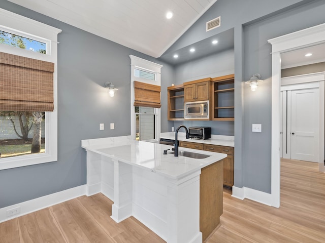 kitchen with a peninsula, brown cabinetry, stainless steel microwave, and open shelves