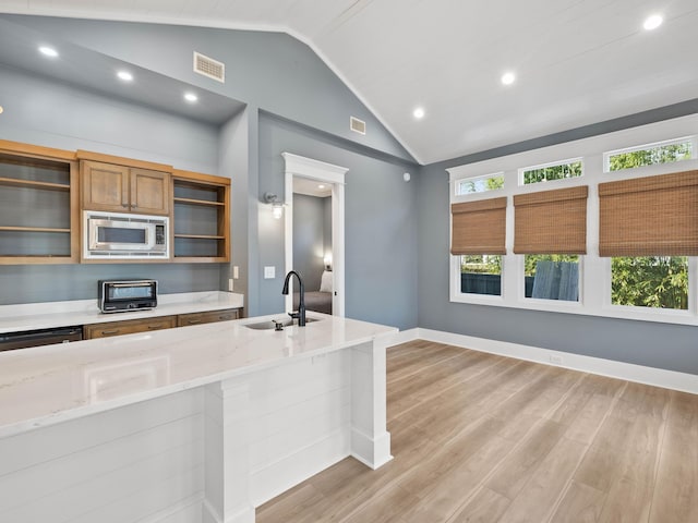 kitchen featuring light stone counters, stainless steel appliances, a sink, brown cabinetry, and glass insert cabinets