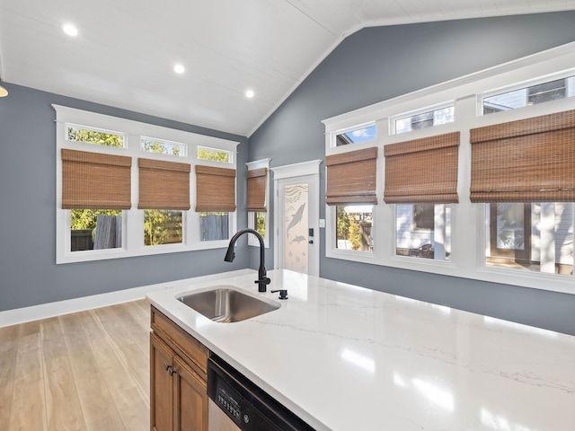 kitchen featuring brown cabinetry, a wealth of natural light, vaulted ceiling, and a sink