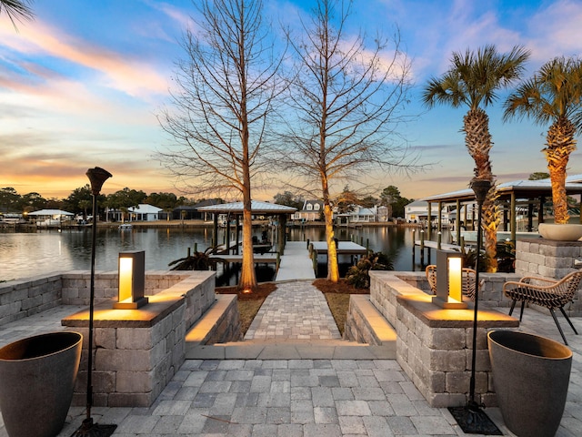 patio terrace at dusk featuring a water view, boat lift, and a boat dock