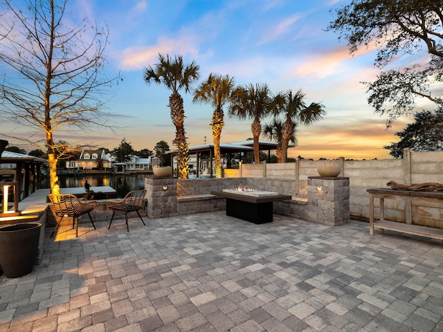 patio terrace at dusk featuring an outdoor living space with a fire pit, a water view, and fence