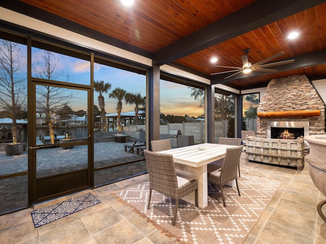 sunroom / solarium with a ceiling fan, wood ceiling, an outdoor stone fireplace, and beam ceiling