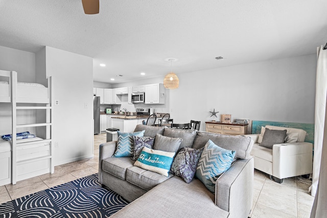 tiled living room with ceiling fan, sink, and a textured ceiling