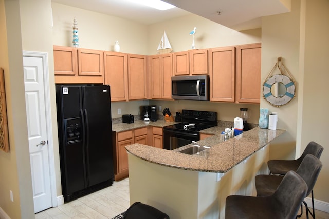 kitchen with black appliances, sink, a kitchen bar, light stone counters, and kitchen peninsula