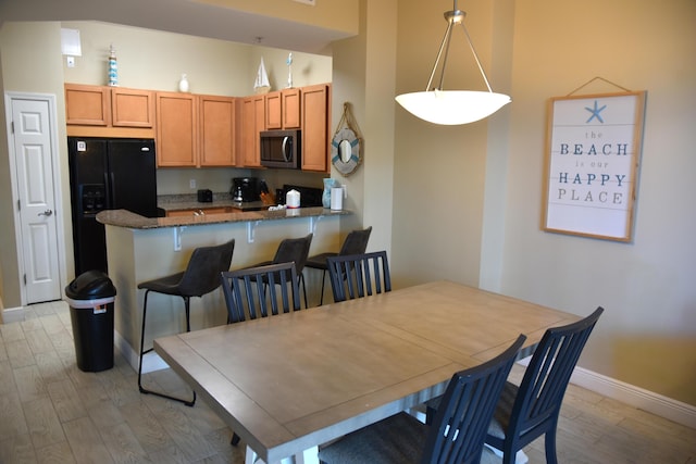 interior space featuring pendant lighting, light hardwood / wood-style flooring, kitchen peninsula, and black fridge