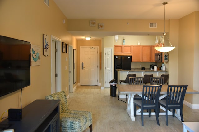 kitchen with hanging light fixtures, light wood-type flooring, and black fridge