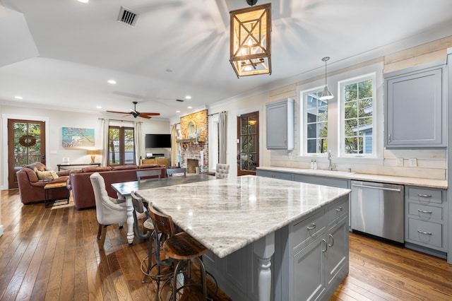 kitchen with a brick fireplace, decorative light fixtures, sink, dishwasher, and a center island