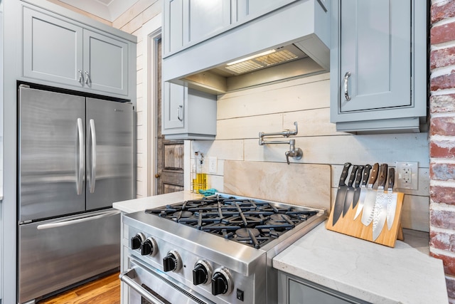 kitchen featuring light stone counters, brick wall, stainless steel appliances, and custom exhaust hood