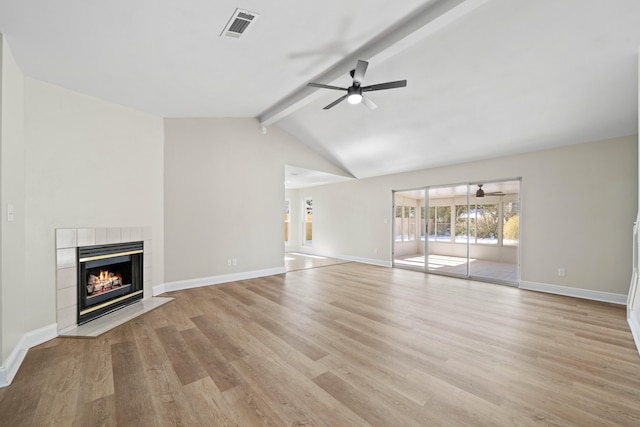 unfurnished living room with ceiling fan, a tiled fireplace, lofted ceiling with beams, and light hardwood / wood-style flooring