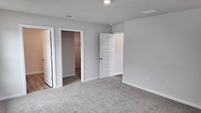 unfurnished bedroom featuring a walk in closet, light carpet, a textured ceiling, and a closet