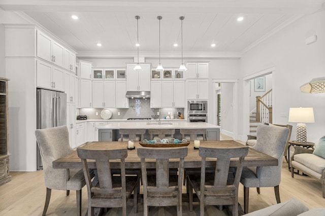 kitchen with pendant lighting, white cabinetry, stainless steel appliances, a center island with sink, and crown molding