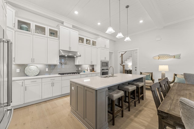 kitchen with white cabinets, stainless steel appliances, an island with sink, hanging light fixtures, and a breakfast bar area