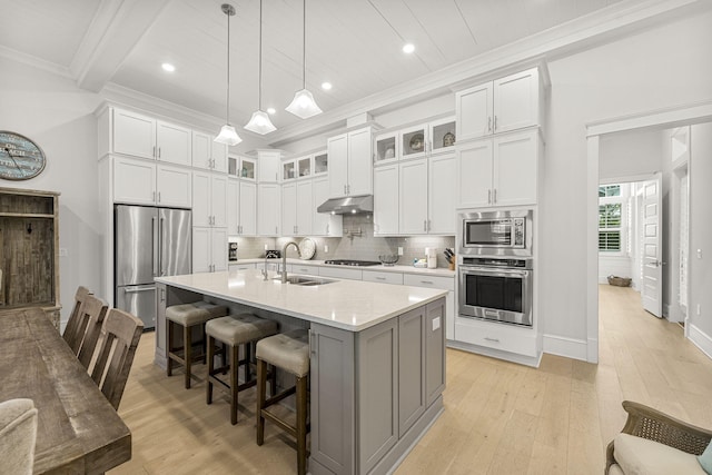 kitchen featuring white cabinetry, a kitchen bar, a center island with sink, stainless steel appliances, and beamed ceiling